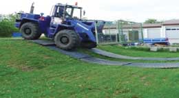 Blue digger driving up hill across ground protection mats laid out on grass
