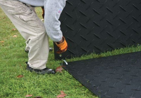 Man fitting a single connector to two black ground protection mats