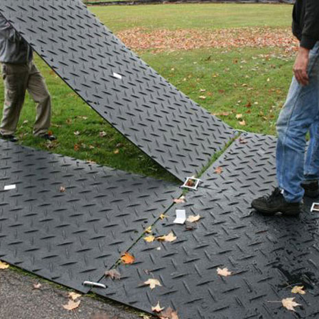Man lowering down a ground protection mat after connecting it to another mat with a double connector