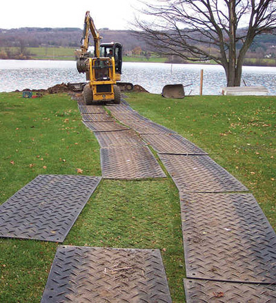 Temporary road matting on grass with one mat moved to show there is no damage to the grass underneath